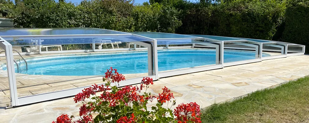 Abri de piscine bas télescopique Vision sans rail installé dans un jardin dans le Var, structure transparente et modules coulissants