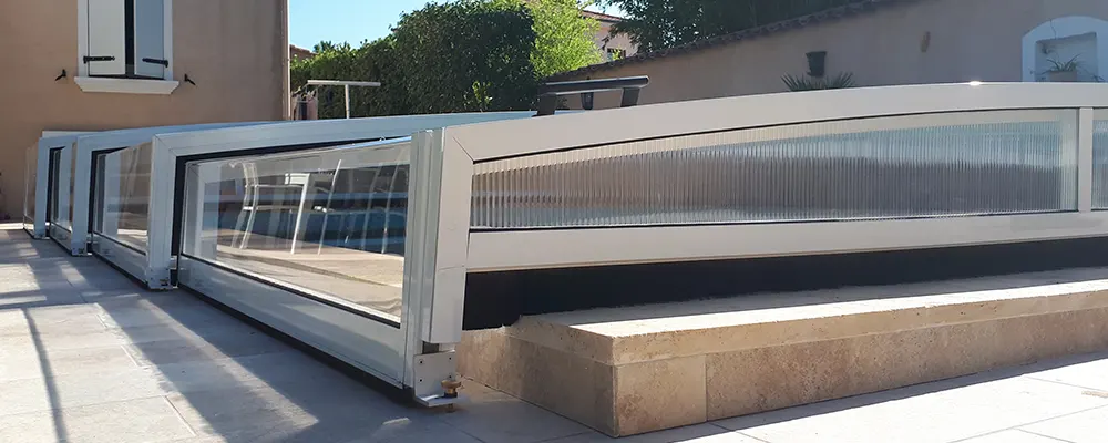 Abri de piscine télescopique bas Atoll avec structure aluminium et panneaux transparents installé en extérieur sans rail apparent